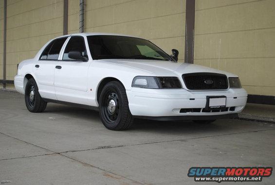 White sedan with black steel wheels and tinted windows parked on concrete. Front grille is black. License plate area is blank