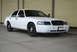 1998 Ford Crown Victoria - White sedan with black steel wheels and tinted windows parked on concrete. The front grille is black and the license plate area is blank.