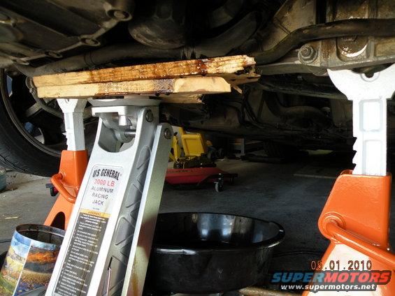 Car underside supported by jack stands and a racing jack, with a drain pan below
