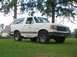 1989 Ford Bronco - A white Ford Bronco is shown from the front-right angle, parked on a grassy lawn with trees in the background.