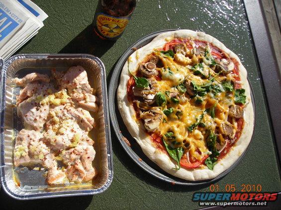 Pizza and chicken in foil pan on green table with bottle and papers
