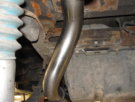 close-up of shiny exhaust pipe curving under rusty vehicle frame