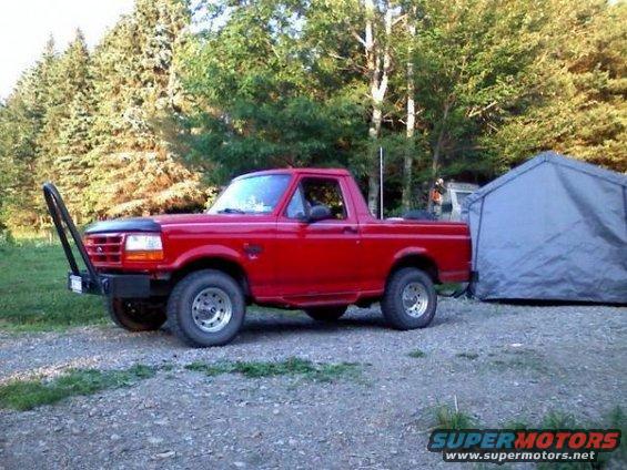 Red pickup truck with a brush guard bumper parked next to a tent
