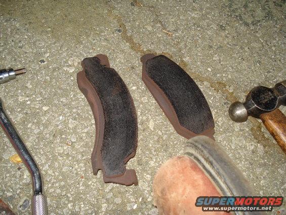 Two brake pads, a hammer, and a wrench on a concrete surface