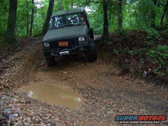 Green Jeep Cherokee XJ driving through a muddy trail in the woods