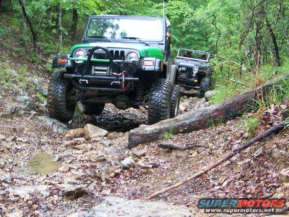 Green Jeep and another Jeep navigating a rough, wooded trail with large rocks and fallen trees