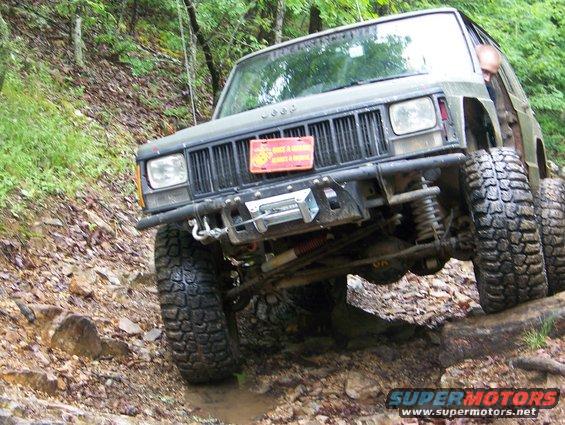 Jeep Cherokee XJ climbing over rocks on a trail. Has a winch and big tires