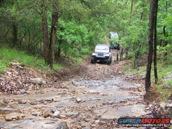 Several Jeeps driving up a rough, rocky, wooded trail