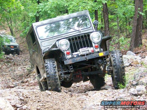 Olive green Jeep CJ-5 navigating a steep, rocky off-road trail with another vehicle behind it
