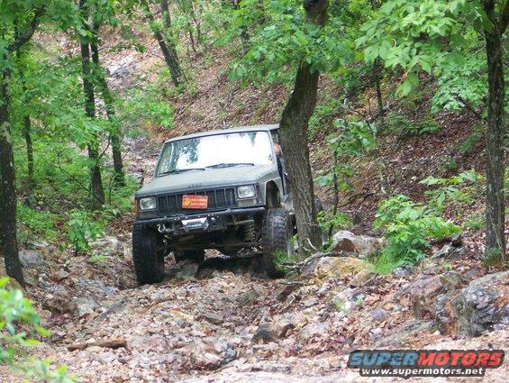 Jeep Cherokee XJ on a rocky trail in the woods. Has a winch and off-road bumper