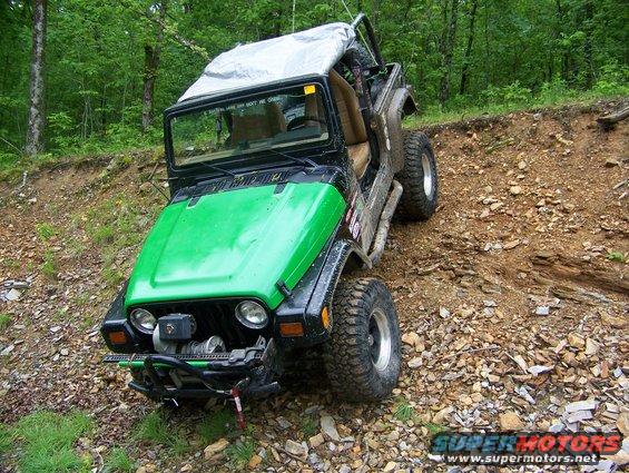 Green Jeep Wrangler on a rocky incline with a tarp over the roll cage