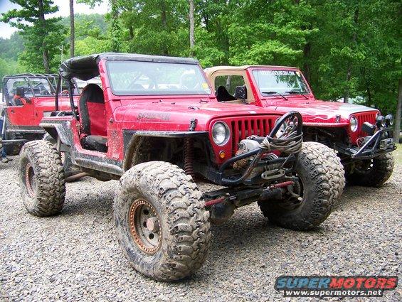 Two red off-road Jeeps with large tires parked on gravel