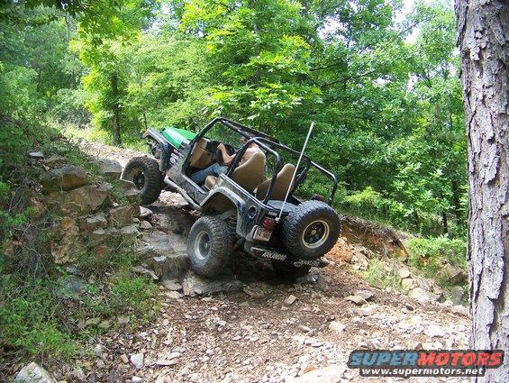 Black Jeep Wrangler with green hood climbing a rocky incline