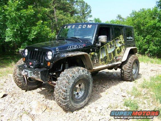 Black Jeep Wrangler JK with "4WS.COM" and "HEMI" decals, lifted with large off-road tires, on a dirt path