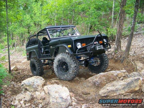 Dark green off-road SUV with large tires on a rocky trail. Appears to be a 1970s Ford Bronco