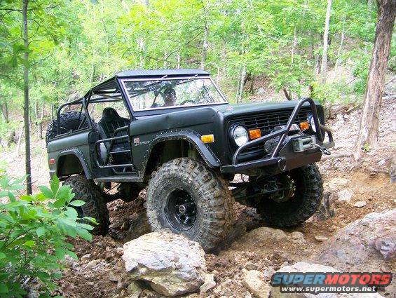 Modified dark green Ford Bronco with roll cage and winch navigating rocky terrain