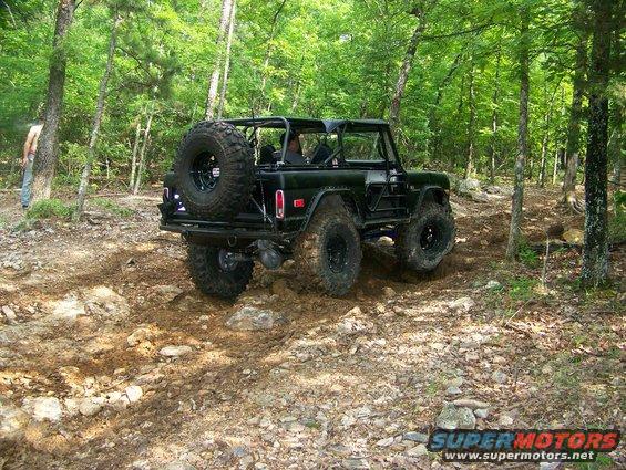 Black off-road SUV with spare tire on back driving on a wooded trail