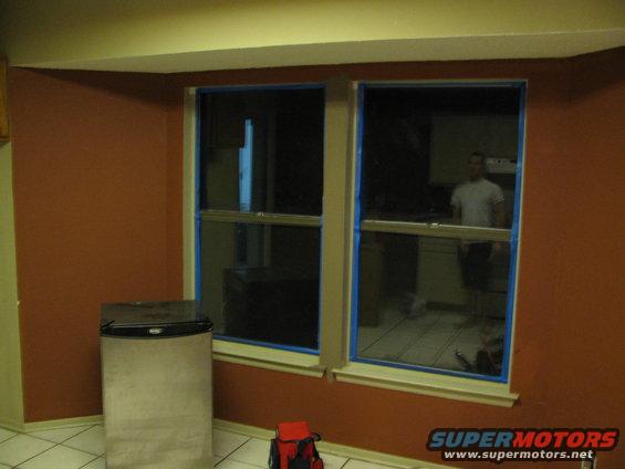 Interior scene with a person reflected in a window, a mini-fridge, and a red bag