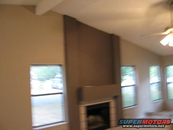 Interior scene with fireplace, vaulted ceiling, and windows showing trees and a street