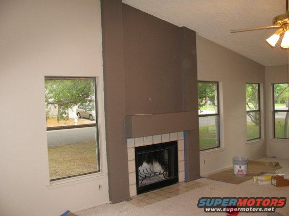 Interior view of a room with a large brown fireplace, multiple windows showing trees and a light-colored vehicle outside
