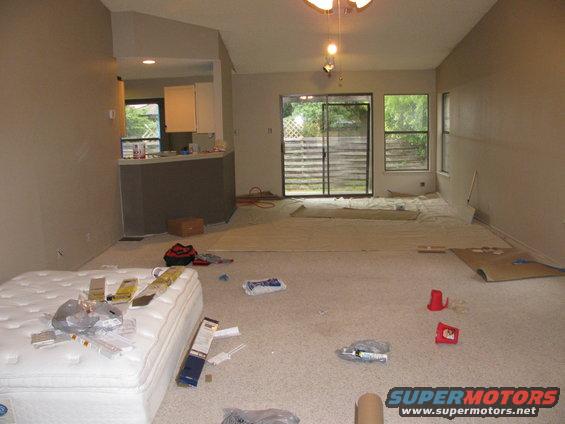 Interior of a room under renovation with a mattress, drop cloths, and construction materials scattered on the floor