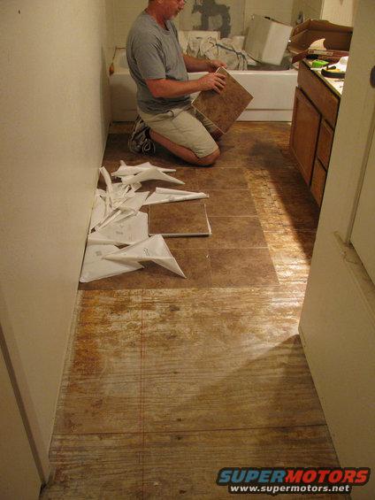 guy kneeling on floor, putting down a tile. Old flooring visible