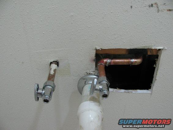 Plumbing pipes and shut-off valves protruding from a textured ceiling