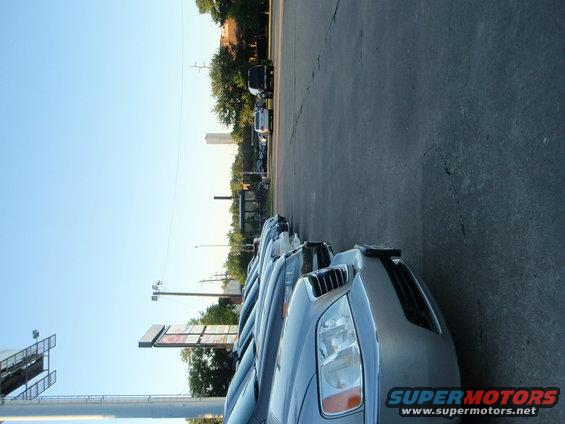Several cars parked in a row, facing forward. A sign with "SUPERMOTORS" is visible on the front car