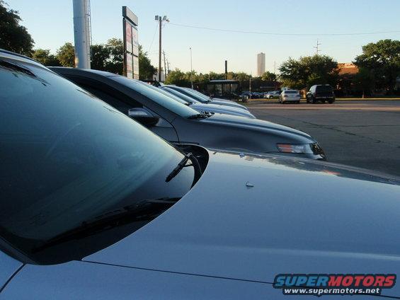 Silver car hood and windshield with other cars parked behind