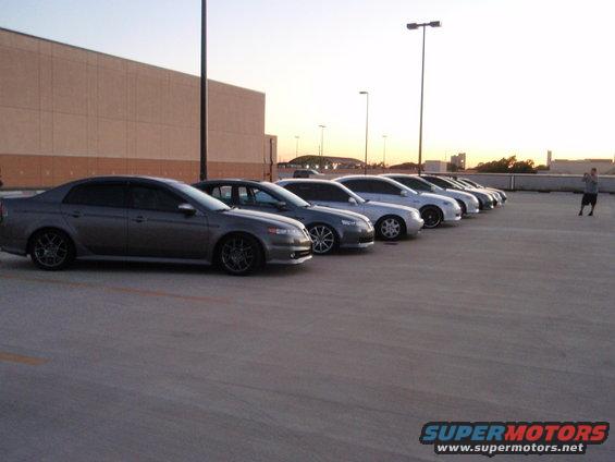 Several Acura sedans parked in a row on a lot, with a person taking a photo in the background