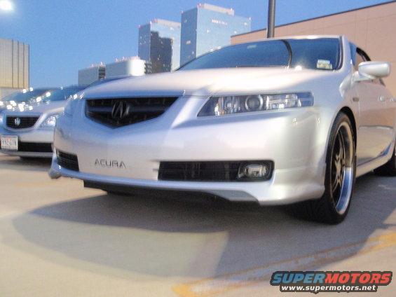 Front view of a silver Acura sedan with aftermarket wheels. Another silver sedan is parked to the left