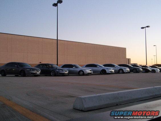 Several sedans parked in a row in front of a large building, with streetlights visible