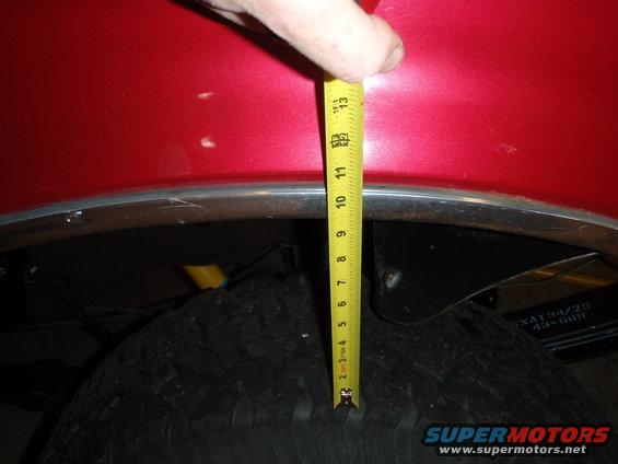 Red vehicle fender with chrome trim above a tire, a yellow tape measure reads 11 inches