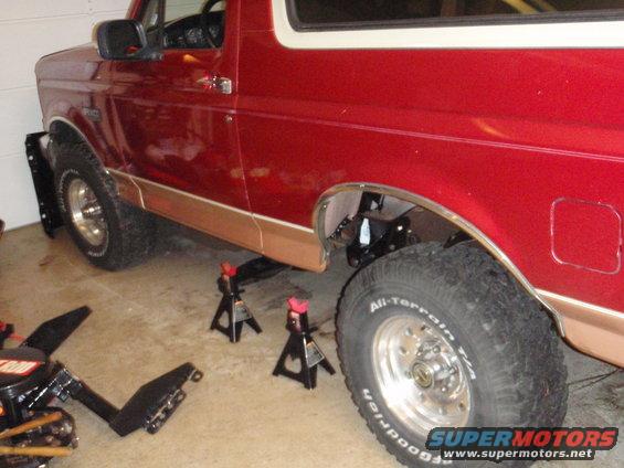 1995 Ford Bronco rear quarter panel and tire, raised on jack stands in a garage
