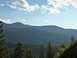 1994 Ford Bronco - A vast landscape of mountains and dense forest stretches under a bright, cloudy sky.