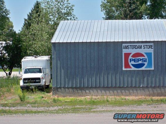 White box truck parked on grass next to a corrugated metal building with a Pepsi sign