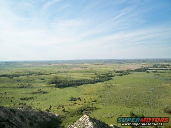 Vast green rolling hills under a blue sky with wispy clouds. A rocky outcrop is in the foreground