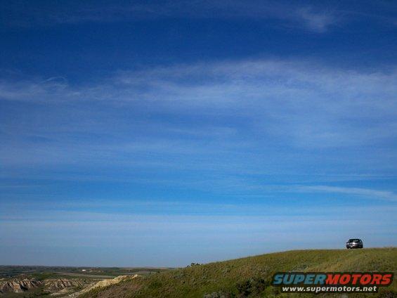 Dark SUV parked on a grassy hilltop with a vast blue sky