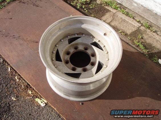 Aluminum wheel with a multi-lug bolt pattern and triangular cutouts in the center, resting on a metal surface