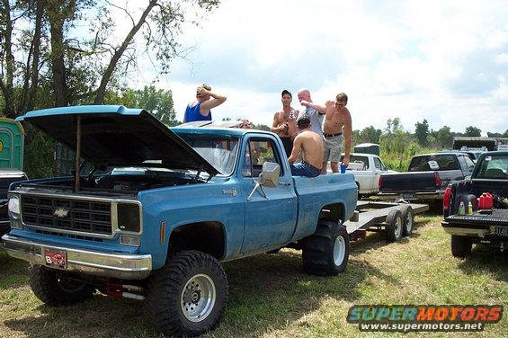 Blue pickup truck with hood open, people in the bed, towing a trailer