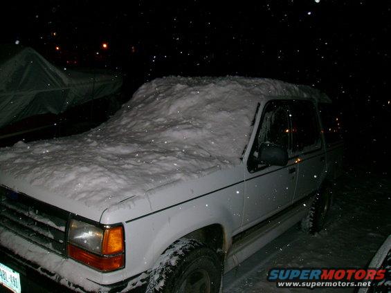 White 1994 Ford Explorer covered in snow, 3/4 front view at night