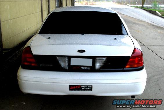 Rear view of a white sedan with tinted windows and a black accent panel between the taillights. It has a 'DARE' sticker on the bumper