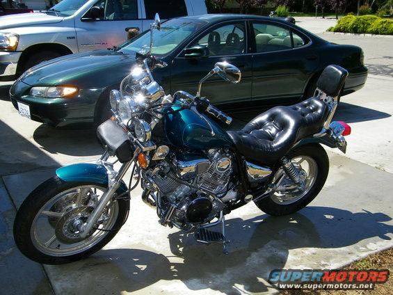 Teal motorcycle with black leather seat parked on concrete, next to a dark green sedan and a silver truck