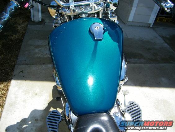 Teal motorcycle gas tank with chrome fuel cap, chrome handlebars, and black seat