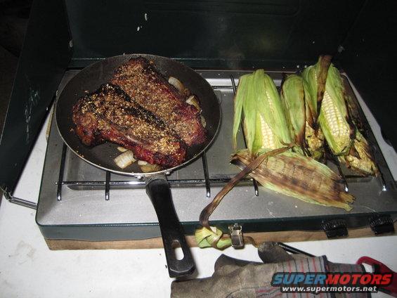 Camping stove with steak in a pan and corn on the cob