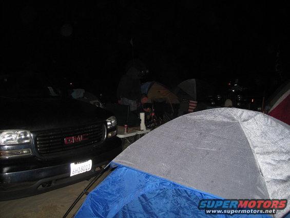 Black GMC truck front end with license plate 6H18012 at a campsite