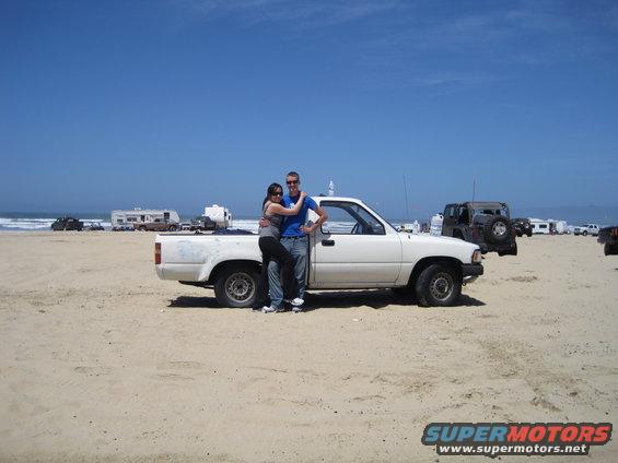 White 1989 Toyota Pickup/SR5 parked on a sandy beach with a couple posing in front of it