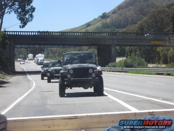 Several Jeep Wranglers driving on a highway under an overpass