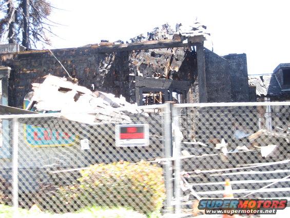 Building destroyed by fire, debris piled up, chain-link fence in foreground