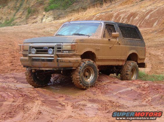 Mud-covered 1991 Ford Bronco with off-road tires driving through mud